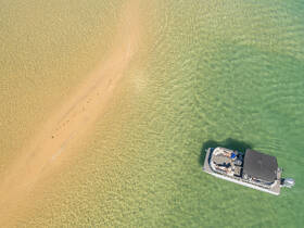 Aerial view of a pontoon boat anchored near a sandbar, with guests enjoying the sun and water — a perfect setting for a relaxing day on the water.