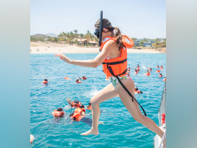 A snorkeler leaps into the vibrant waters, joining a group of adventurers in life jackets, ready for an exciting underwater exploration.