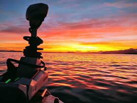 A silhouette of a device against a vibrant sunset over calm waters, creating an atmospheric scene.