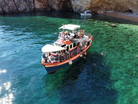 A vibrant scene of guests enjoying a day on the water, with a boat anchored in clear turquoise waters and people swimming nearby — perfect for a fun-filled beach adventure.