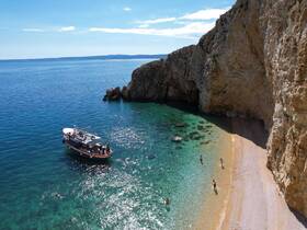 A scenic view of a boat anchored near a beautiful beach, with people enjoying the water — a perfect spot for relaxation and fun in the sun.