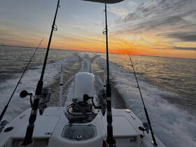 A stunning sunset view from the helm of a fishing boat, showcasing the tranquil waters and the thrill of a fishing adventure.