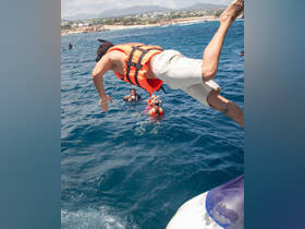 A thrilling moment captured as a person jumps into the vibrant blue waters, with friends enjoying snorkeling nearby — perfect for adventure seekers on a fun day out at sea.