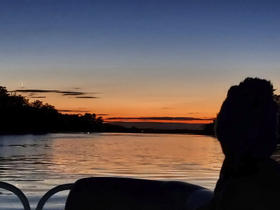 A serene sunset view over calm waters, with a silhouette of a person enjoying the tranquil atmosphere aboard a boat — perfect for evening cruises.