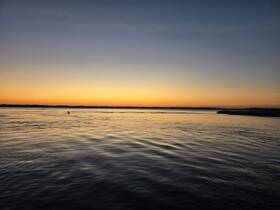 A serene sunset over calm waters, with a silhouette of a person enjoying the tranquil scenery — perfect for capturing the beauty of nature during evening boat trips.