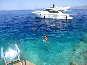 A lively scene of guests enjoying a refreshing swim in crystal-clear waters, with a luxurious boat anchored nearby — perfect for summer adventures and fun on the water.