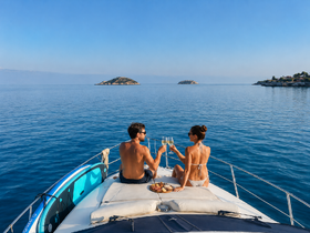 A couple toasts with glasses of champagne while enjoying a serene moment on the deck of a yacht, surrounded by stunning islands — an idyllic setting for romantic getaways.