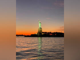 A stunning sunset view of the Statue of Liberty reflecting in the water, showcasing one of New York City's most iconic landmarks.