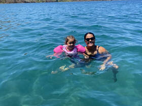 A joyful moment captured as a mother and her child swim together in clear waters, showcasing a delightful family experience in nature.