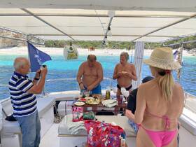A lively group enjoys a meal preparation on a boat, capturing moments of fun and camaraderie against a stunning turquoise backdrop.