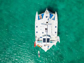 Aerial view of a catamaran cruising through crystal-clear turquoise waters, showcasing its spacious deck and vibrant water toys, perfect for adventurous outings.