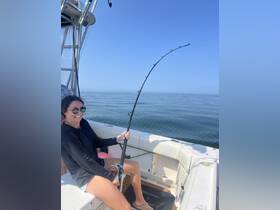 A joyful angler enjoys a fishing experience on a boat, showcasing the thrill of reeling in a catch on a sunny day at sea.