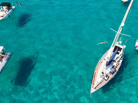 A vibrant scene of guests enjoying the clear waters while swimming near a sailboat, showcasing the perfect day for sailing and water activities.