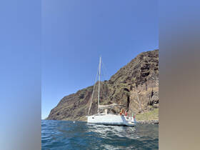 A serene view of a catamaran docked near a rocky coastline, showcasing the vessel's sleek design against a clear blue sky.