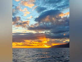 A breathtaking sunset over the ocean, with vibrant colors illuminating the sky and a distant coastline, perfect for capturing the beauty of nature during a boat trip.
