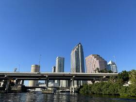 A scenic view of a vibrant city skyline along the waterway, showcasing modern architecture and a clear blue sky — perfect for urban exploration and sightseeing tours.