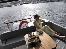 A woman enjoys a refreshing cocktail while relaxing on the deck of a boat, surrounded by delicious food — perfect for a luxurious day on the water.