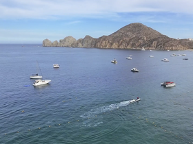 A scenic view of multiple boats anchored in calm waters, with a jet ski in action, showcasing the vibrant marine life and coastline — perfect for water sports enthusiasts.
