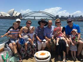 A joyful family gathers on a boat in Sydney, with the iconic Sydney Opera House and Harbour Bridge in the background, perfect for memorable outings and celebrations.