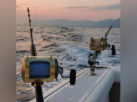 Close-up of fishing rods and reels on a boat, set against a beautiful sunset backdrop — perfect for deep-sea fishing adventures.
