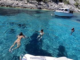 A group enjoys snorkeling in crystal-clear waters, with a boat anchored nearby, creating the perfect setting for aquatic adventures.