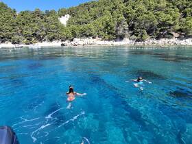 Two children enjoy a refreshing swim in the crystal-clear waters of a picturesque beach, surrounded by lush greenery — a perfect summer getaway.