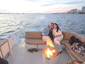 A couple enjoys a romantic moment on a boat at sunset, cozying up by a fire pit — an ideal setting for intimate evening cruises.