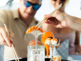Guests enjoy beautifully presented sushi and cocktails aboard a boat, showcasing the perfect dining experience on the water.