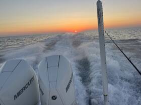 A stunning sunset view from the back of a speedboat, showcasing the powerful Mercury engines and the wake created as it speeds through the water.