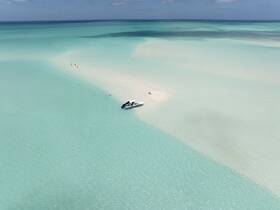 A stunning aerial view of a boat anchored near a sandbar, with people enjoying the shallow waters — a perfect scene for beach lovers and adventure seekers.