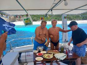 A lively group enjoys a delicious spread of snacks aboard a boat, surrounded by stunning turquoise waters — perfect for a fun day out on the sea.