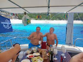 Two friends enjoy a meal and drinks on a boat, surrounded by stunning turquoise waters — a perfect moment of relaxation and celebration on the water.