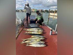 Two fishermen proudly display their catch of the day on the dock, showcasing a variety of fish after a successful fishing trip.