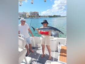 A woman proudly displays her catch while fishing on a boat, with a scenic backdrop of the marina — a perfect moment for fishing enthusiasts.