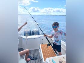 A young boy proudly holds up a fishing rod with a catch while enjoying a day on the water — a perfect family fishing adventure.