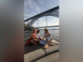 A group of friends relaxes on a boat under a stunning bridge, enjoying a beautiful day on the water — perfect for social outings and memorable experiences.