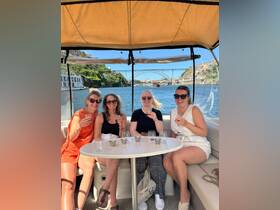 A group of friends enjoys cocktails on a boat, celebrating with drinks while taking in the scenic views of the river and surrounding architecture.
