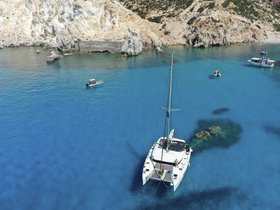 A stunning aerial view of a catamaran anchored in crystal-clear waters, surrounded by rocky cliffs and other boats, perfect for exploring secluded destinations.