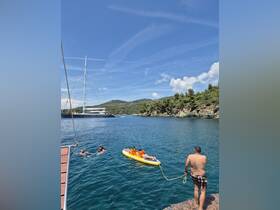 A family enjoys a sunny day on the water, with children on a paddleboard and adults swimming nearby — a perfect summer adventure in a beautiful setting.