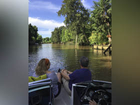 A couple enjoys a serene moment on a boat, surrounded by lush greenery along a tranquil river — perfect for a relaxing day on the water.