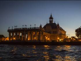 A nighttime view of a beautifully lit structure by the water, creating a serene atmosphere. The image captures the essence of evening boat tours.