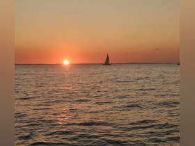 A serene sunset over the ocean with a sailboat silhouetted against the vibrant sky, perfect for capturing the beauty of evening cruises.