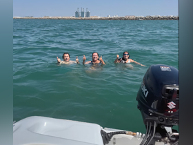 A group of friends enjoys a refreshing swim in the ocean, giving thumbs up to capture the fun of their boating adventure.