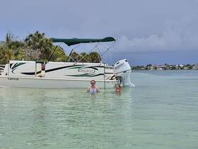 Two friends enjoy a refreshing swim next to their Beachcat boat in crystal-clear waters, capturing the essence of a perfect day on the water.