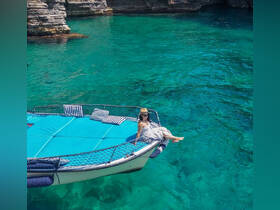 A woman relaxes on the bow of a boat, enjoying the stunning turquoise waters under the sun — a perfect moment for leisure and tranquility on the water.