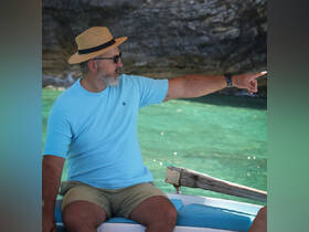 A man gestures while seated on a boat, enjoying the scenic turquoise waters — a perfect moment of exploration and adventure on the water.