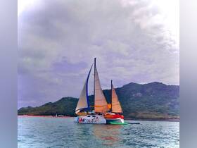 A vibrant catamaran sails through calm waters, showcasing its colorful sails against a scenic backdrop of hills — perfect for leisurely cruises and island adventures.