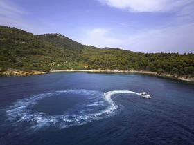 An aerial view of a boat making a sharp turn in crystal-clear waters, surrounded by lush greenery and a scenic coastline — perfect for showcasing thrilling boating adventures.