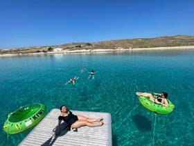 A lively group enjoys a sunny day in crystal-clear waters, with some swimming and others relaxing on inflatable floats — a perfect summer getaway.