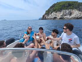 A lively group enjoys a toast aboard a boat, celebrating with drinks against a stunning coastal backdrop — perfect for summer outings and boat parties.